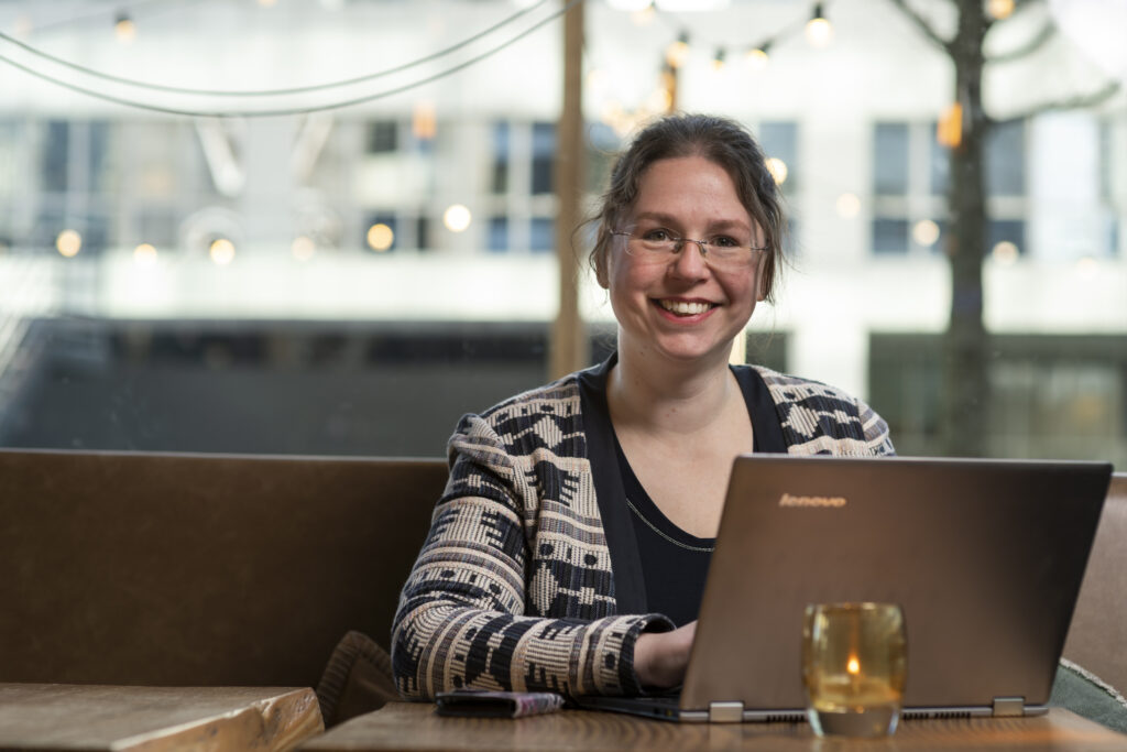 Saskia werkt met haar laptop en kijkt bezoekers lachend aan